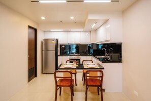 A compact kitchen with white cabinets, a black countertop, and a dining area with two wooden chairs. - Casa Honore Condominium Iloilo City (Iloilo City)