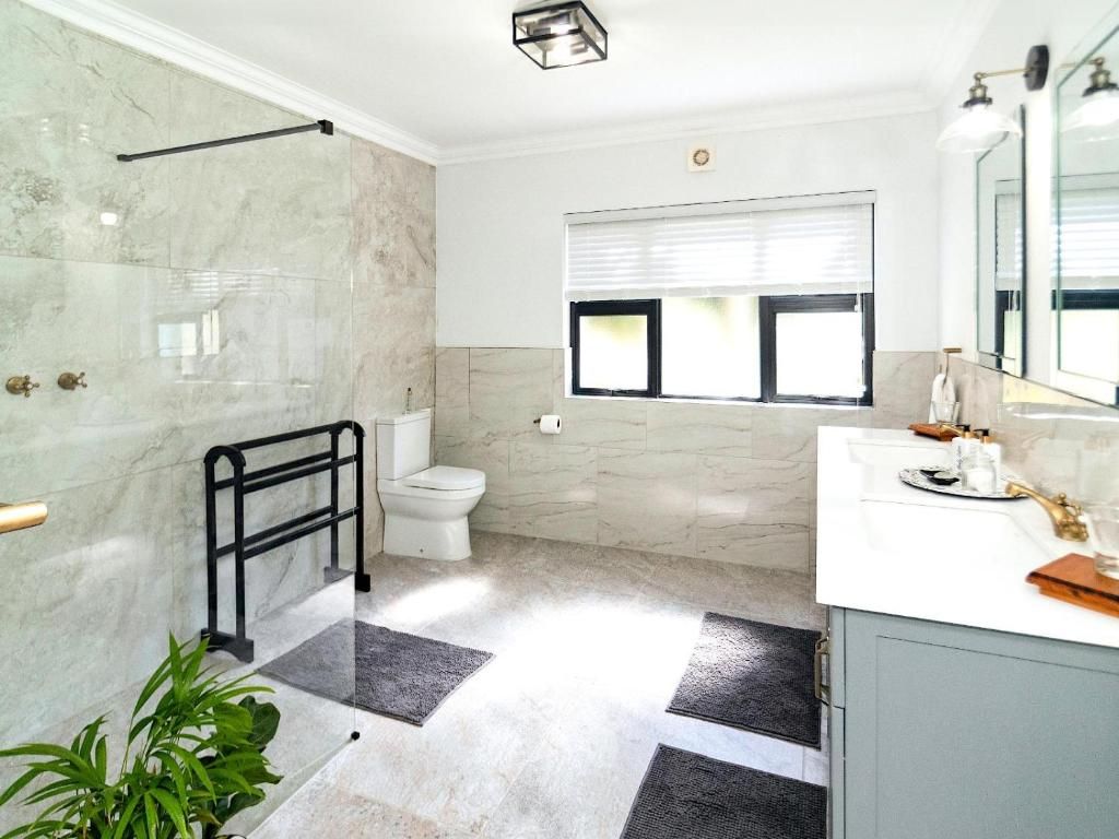 Un bagno con box doccia in vetro, un water, un lavandino con specchio e una finestra con persiane.