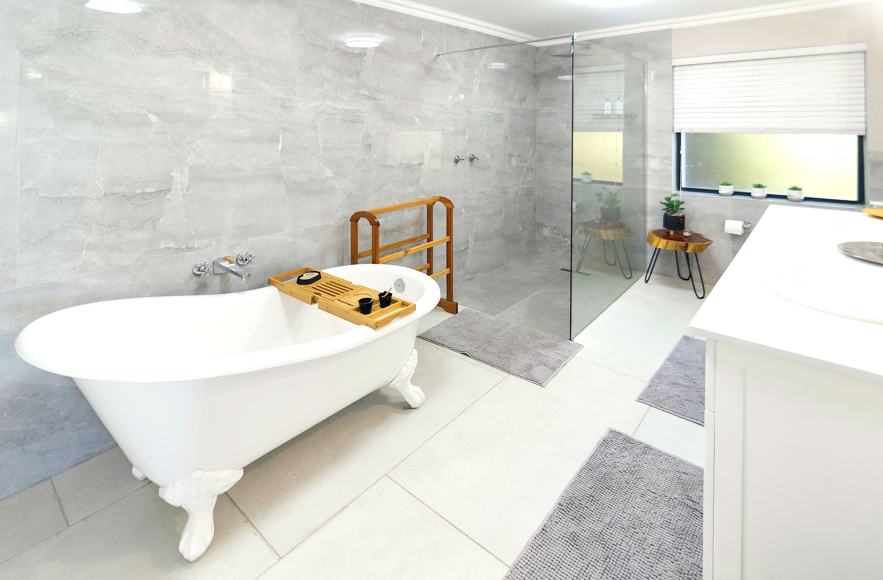 A modern bathroom with a freestanding bathtub, a glass shower enclosure, and a small wooden stool.
