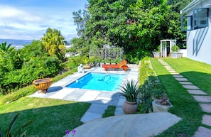 A backyard with a swimming pool, a wooden deck, and a garden area. - Sunnymeade Guest House (Knysna)