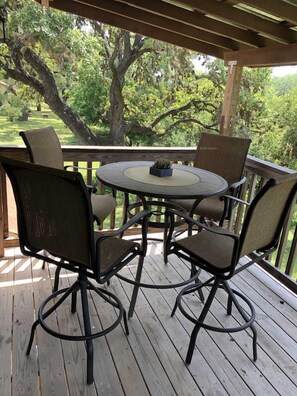 Une terrasse en bois avec une table ronde et quatre chaises, entourée d’une balustrade en bois.