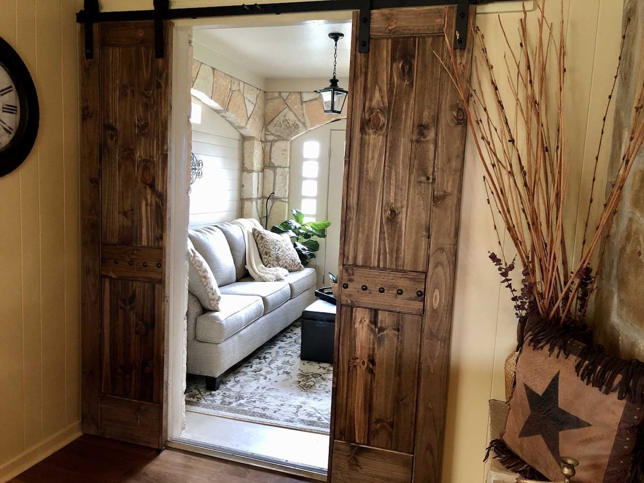 Un interior rústico con una puerta corrediza de madera que da a un espacio de estar con un sofá y un jarrón decorativo.