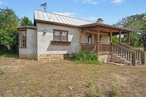 A rustic two-story house with a porch and a stone foundation. - Felix Cabin at Restoration Ranch (Fredericksburg)