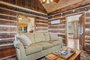 A log cabin interior with a sofa, a tray table, and a sign on the wall. - Felix Cabin at Restoration Ranch (Fredericksburg)