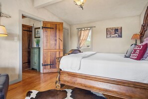 A bedroom with a wooden bed, a cowhide rug, a wooden wardrobe, a lamp, and a painting on the wall. - Freida Cabin at Restoration Ranch (Fredericksburg)