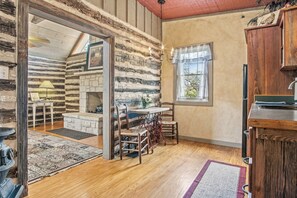A rustic cabin interior with a stone fireplace, wooden dining table, and a window with curtains. - Freida Cabin at Restoration Ranch (Fredericksburg)