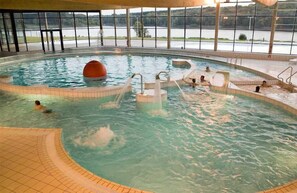 An indoor swimming pool with clear water, multiple entry points, and a view of a lake through large windows.