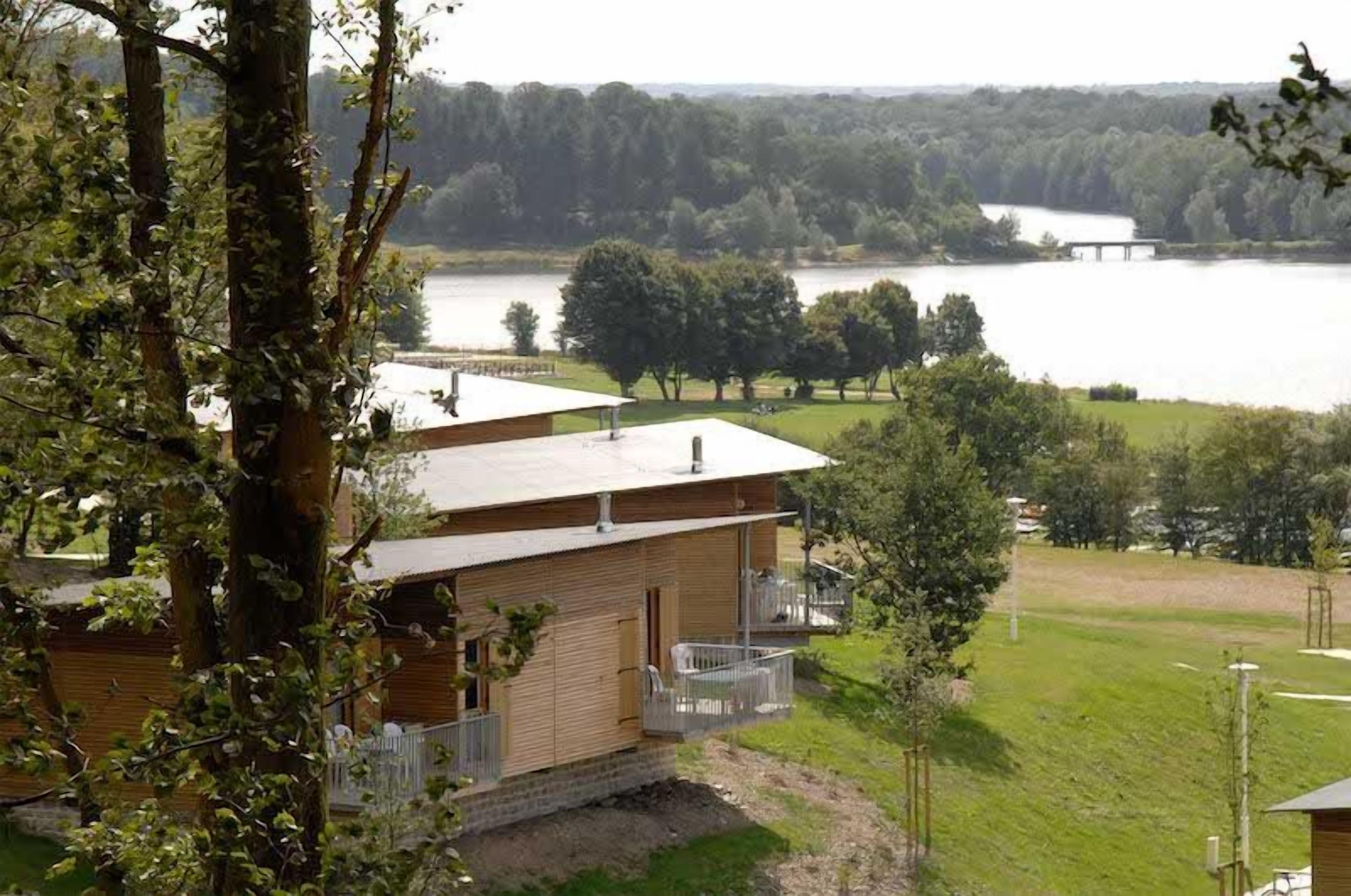 Een chalet met een balkon met uitzicht op een meer, omringd door bomen en een gazon.