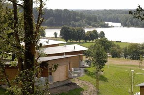 A cabin with a balcony overlooking a lake, surrounded by trees and a grassy area.