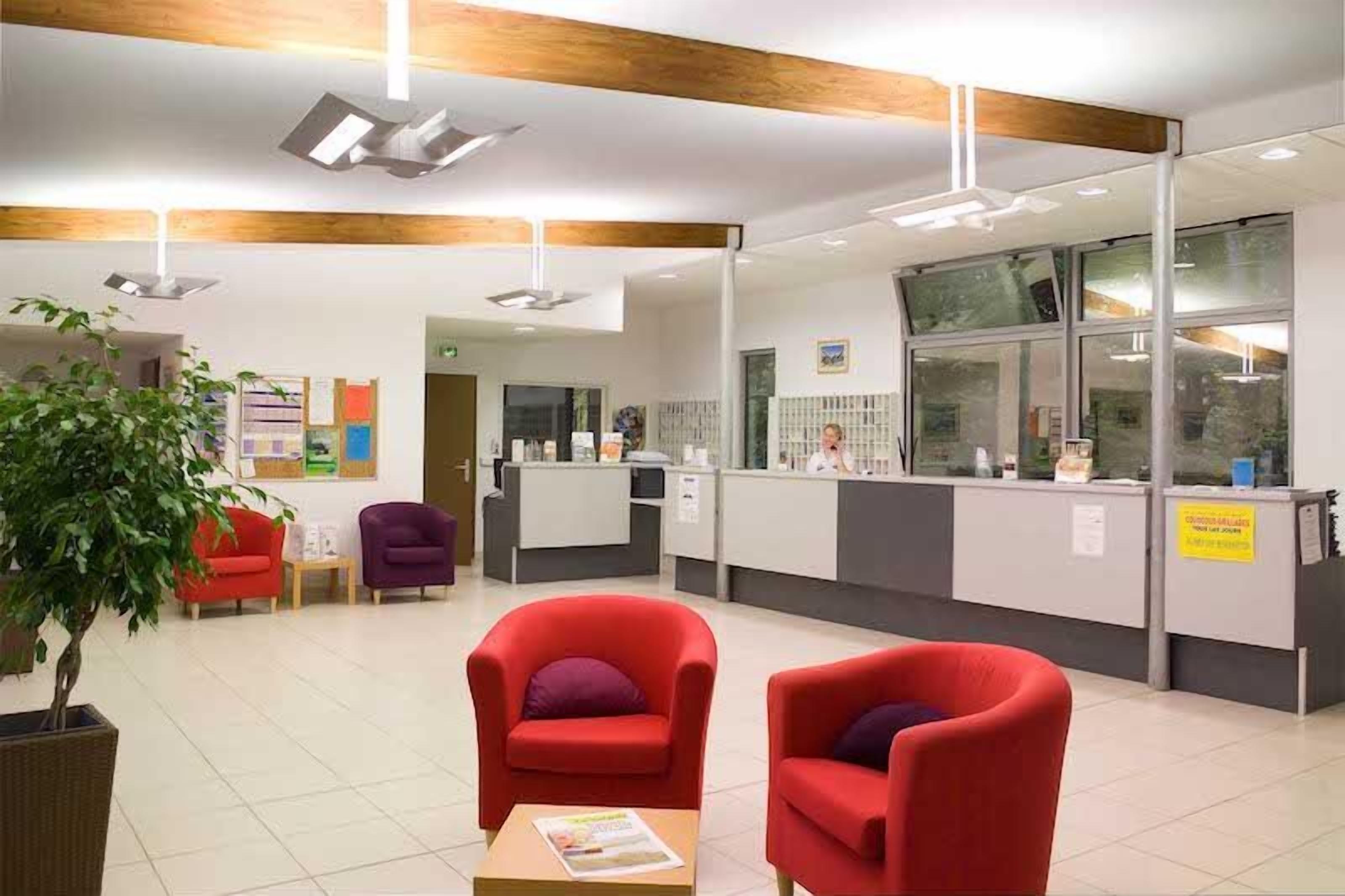 A reception area with a counter, red armchairs, a potted plant, and a bulletin board.