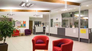 A reception area with a counter, red armchairs, a potted plant, and a bulletin board.