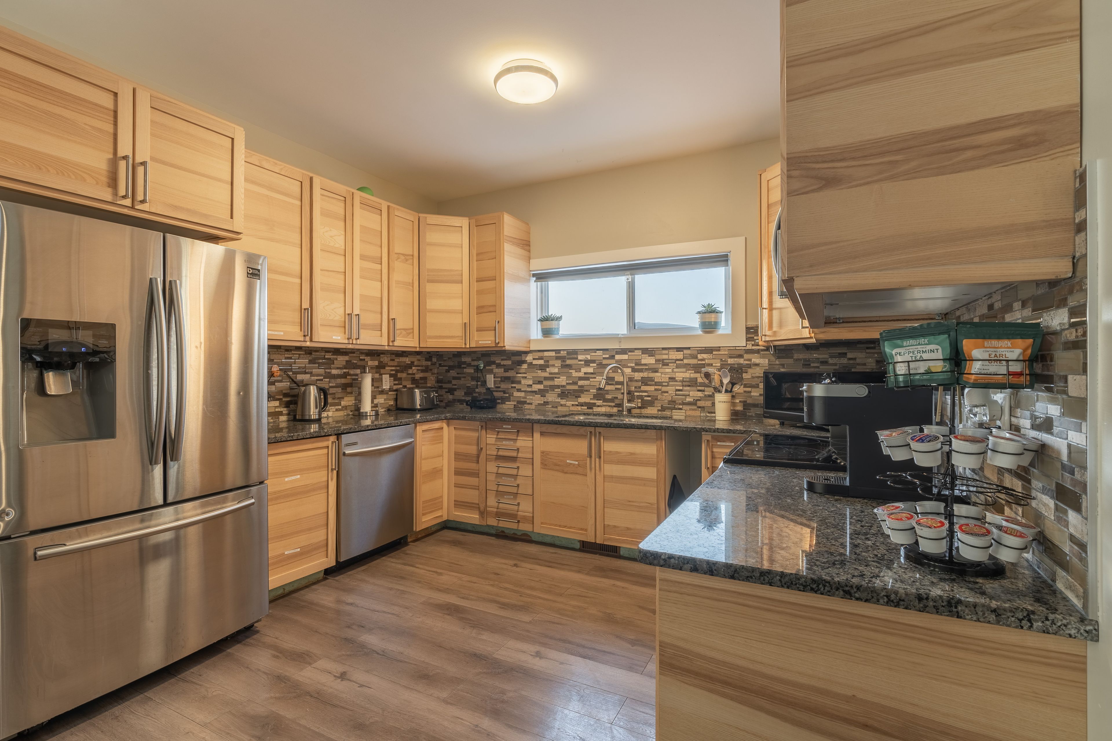 A modern kitchen with wooden cabinets, a stainless steel refrigerator, a built-in oven, and a window above the sink.