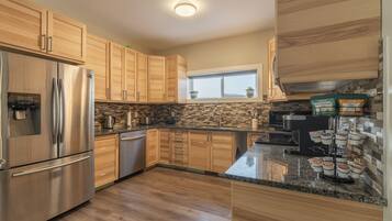 A modern kitchen with wooden cabinets, a stainless steel refrigerator, a built-in oven, and a window above the sink.