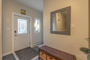 A hallway with a white door, a glass door with a geometric pattern, a wall-mounted mirror, and a bench with a woven basket. - Spacious , luxurious home for comfort, privacy and convenience. Great for Aurora (Yellowknife)