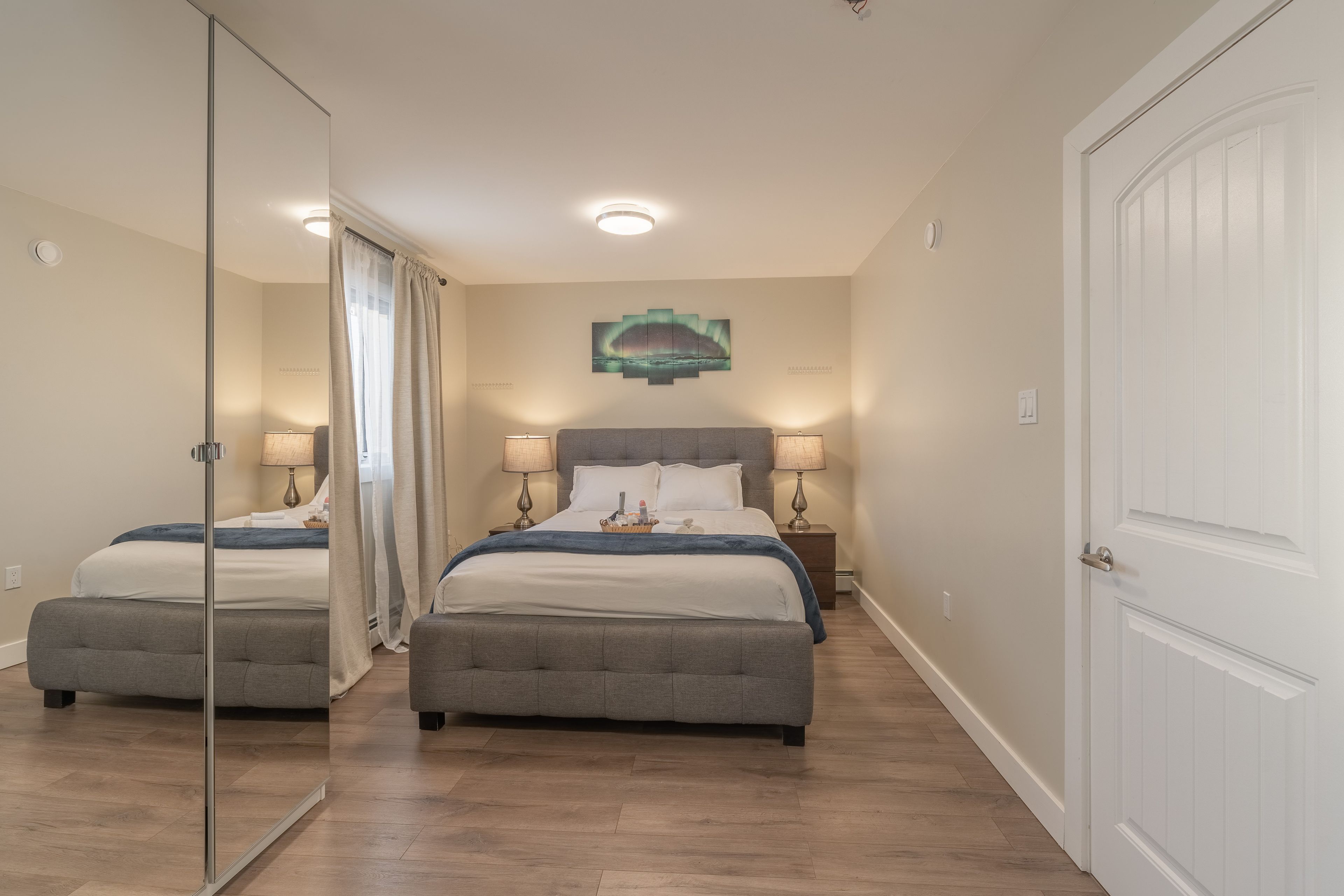 A hotel room with a double bed, two bedside tables with lamps, a mirror, and a door.
