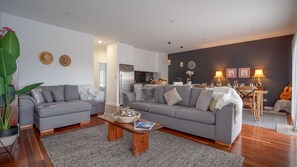 Ein modernes Wohnzimmer mit zwei grauen Sofas, einem Couchtisch und einem Essbereich mit einer Gitarre.