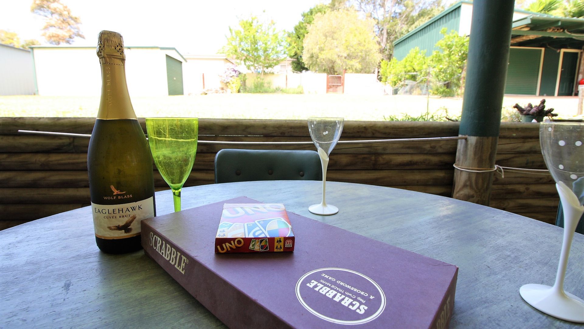 A table with a bottle of Eaglehawk Cuvee Brut wine, a Scrabble game, and two empty wine glasses.