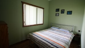 A bedroom with a single bed, a window with blinds, a wooden wardrobe, and a wall with three framed pictures. - Cherry Street Cottage (Bendalong)