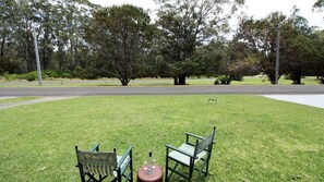 A grassy area with two green chairs and a small table, surrounded by trees. - Cherry Street Cottage (Bendalong)