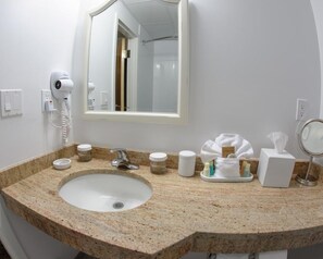 Casa de banho com lavatório bancada em granito, secador de cabelo, espelho e artigos de higiene pessoal.