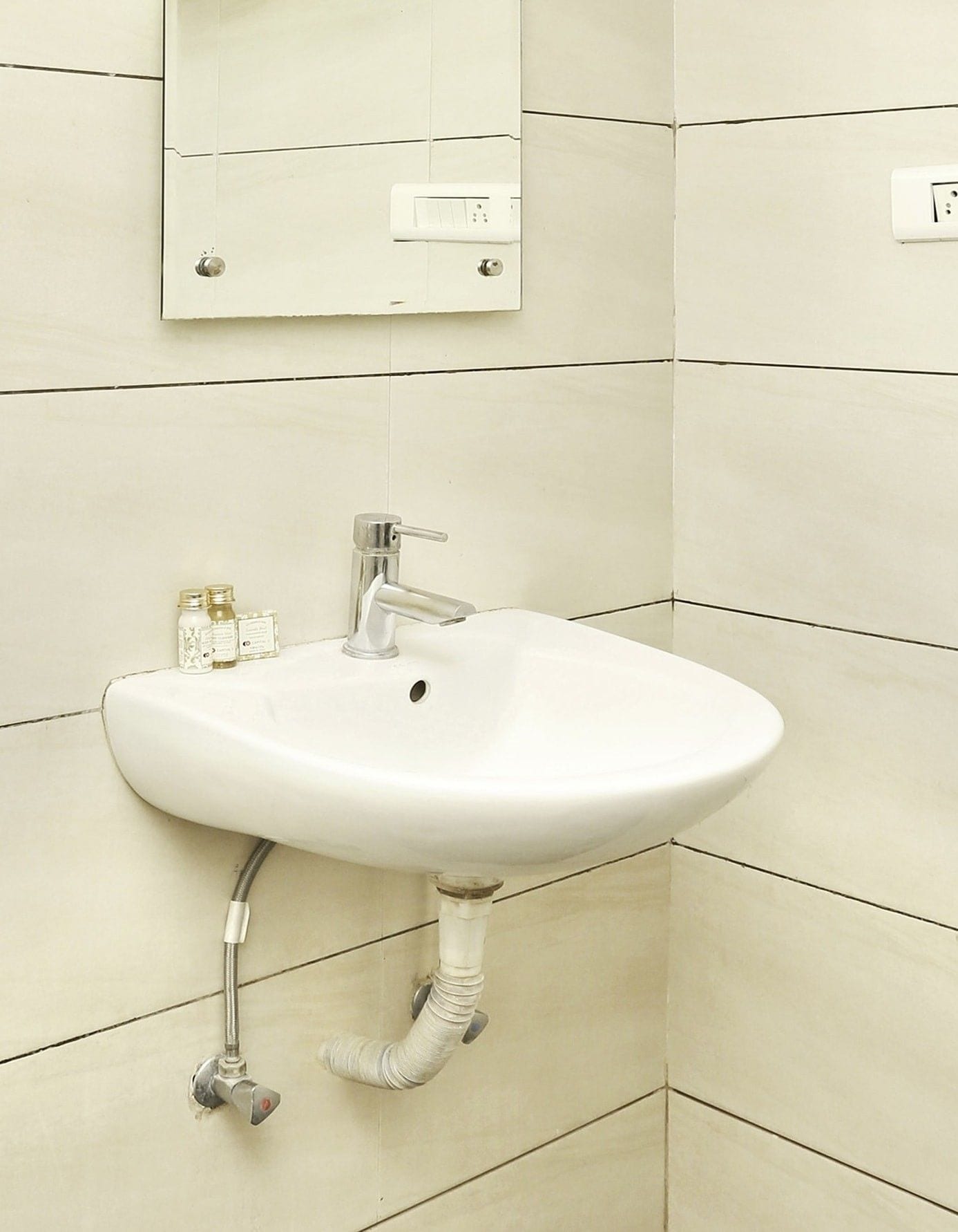 A bathroom with a white sink, a mirror, and a wall-mounted light switch.