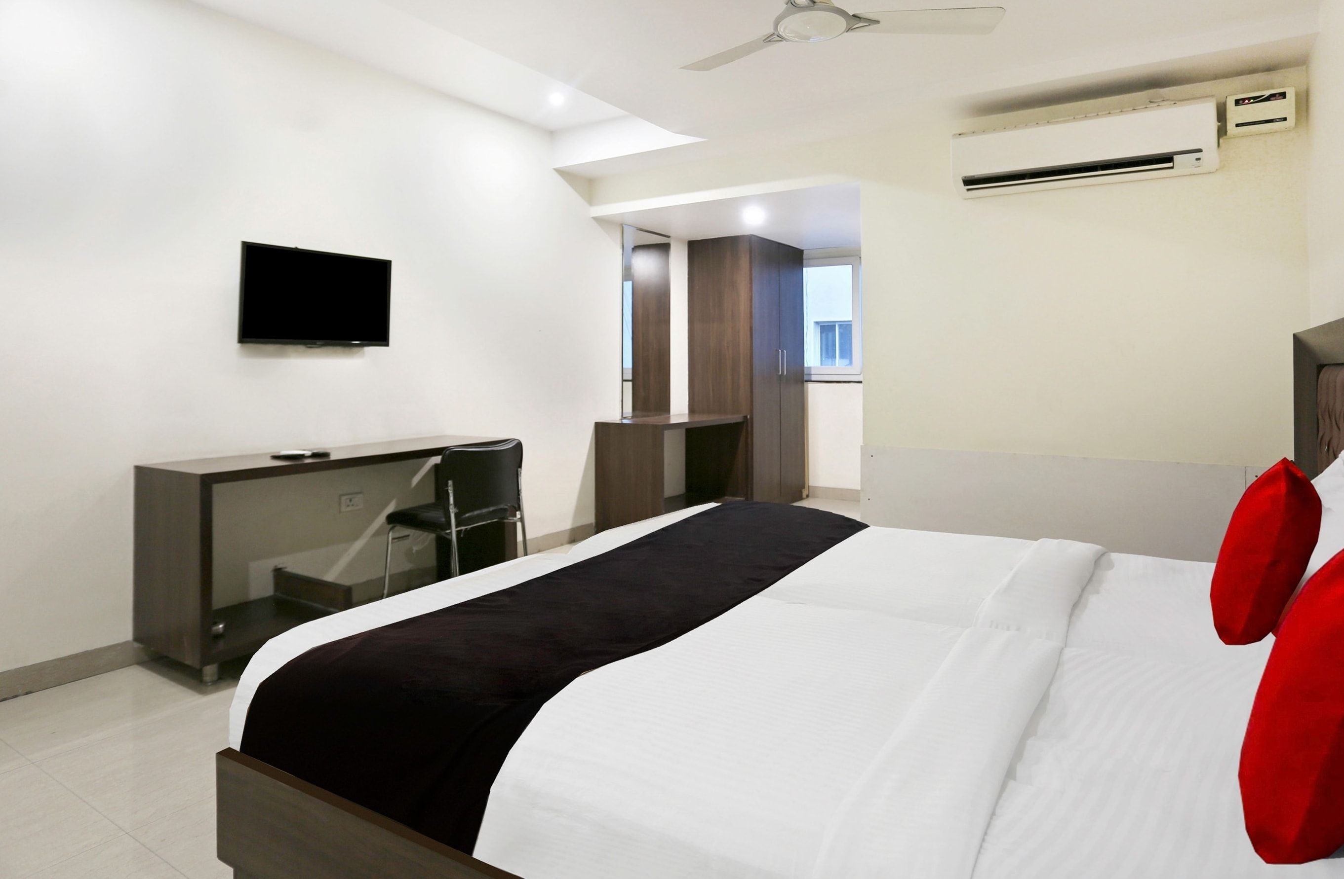 A hotel room with a bed, a desk, a television, and an air conditioning unit.