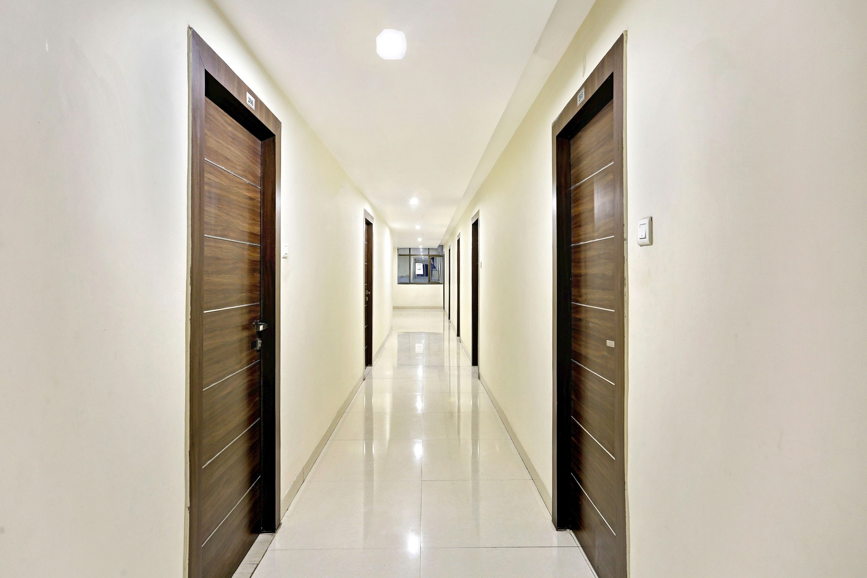 A corridor with doors on both sides, a tiled floor, and a ceiling with recessed lighting.