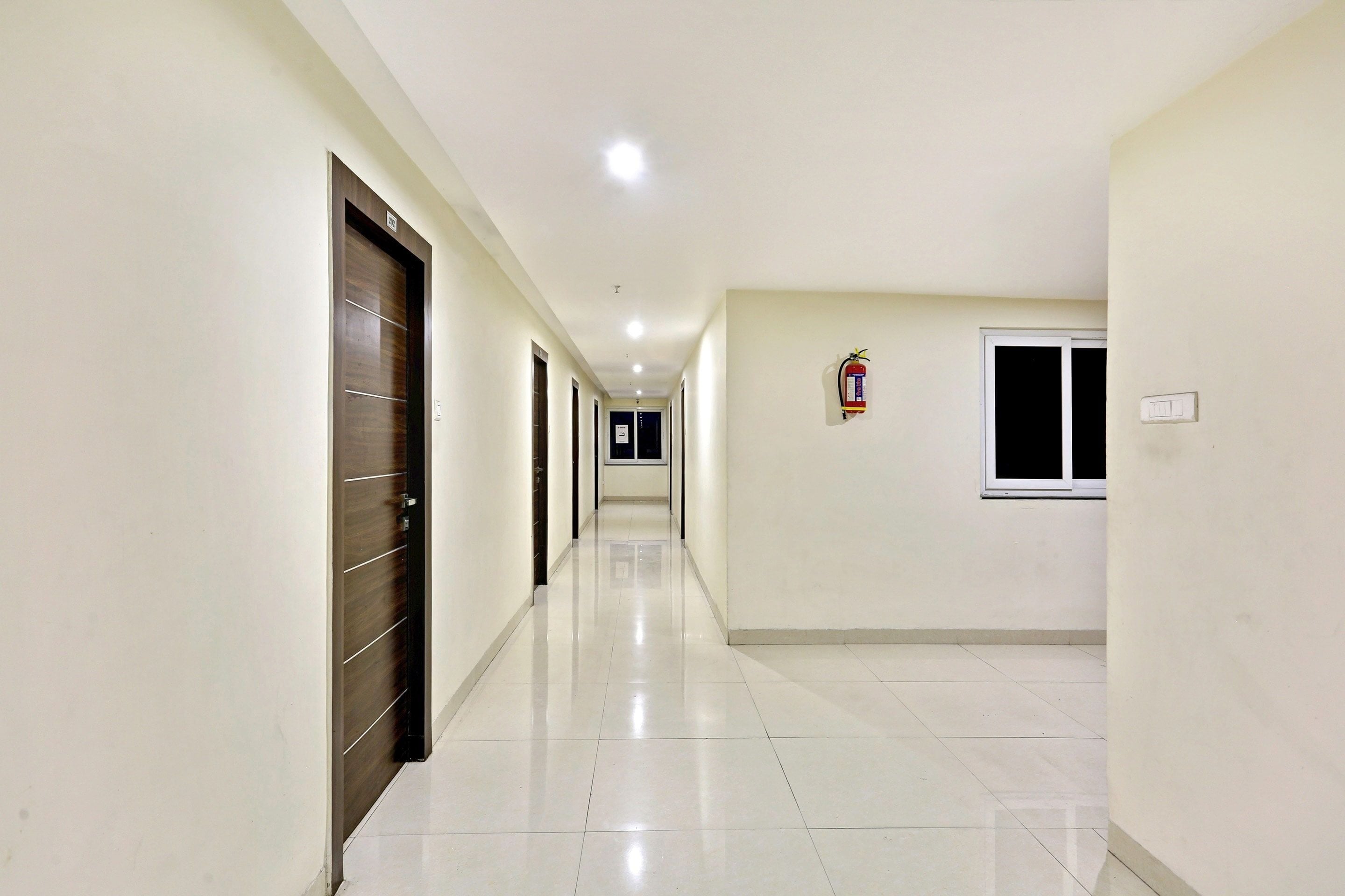 A long, narrow hallway with doors on one side and a window on the other.