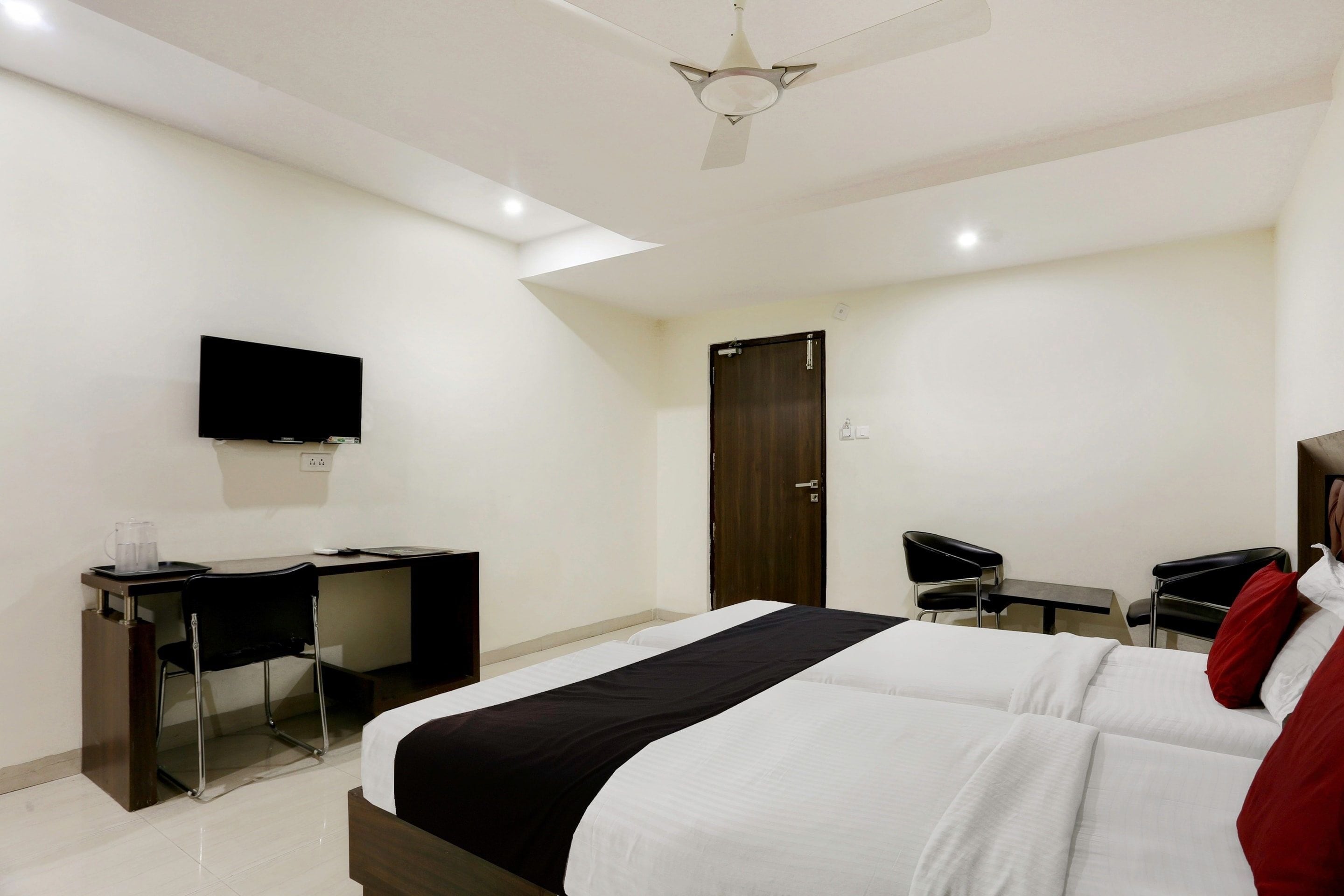 A hotel room with a bed, desk, chair, television, and a door.