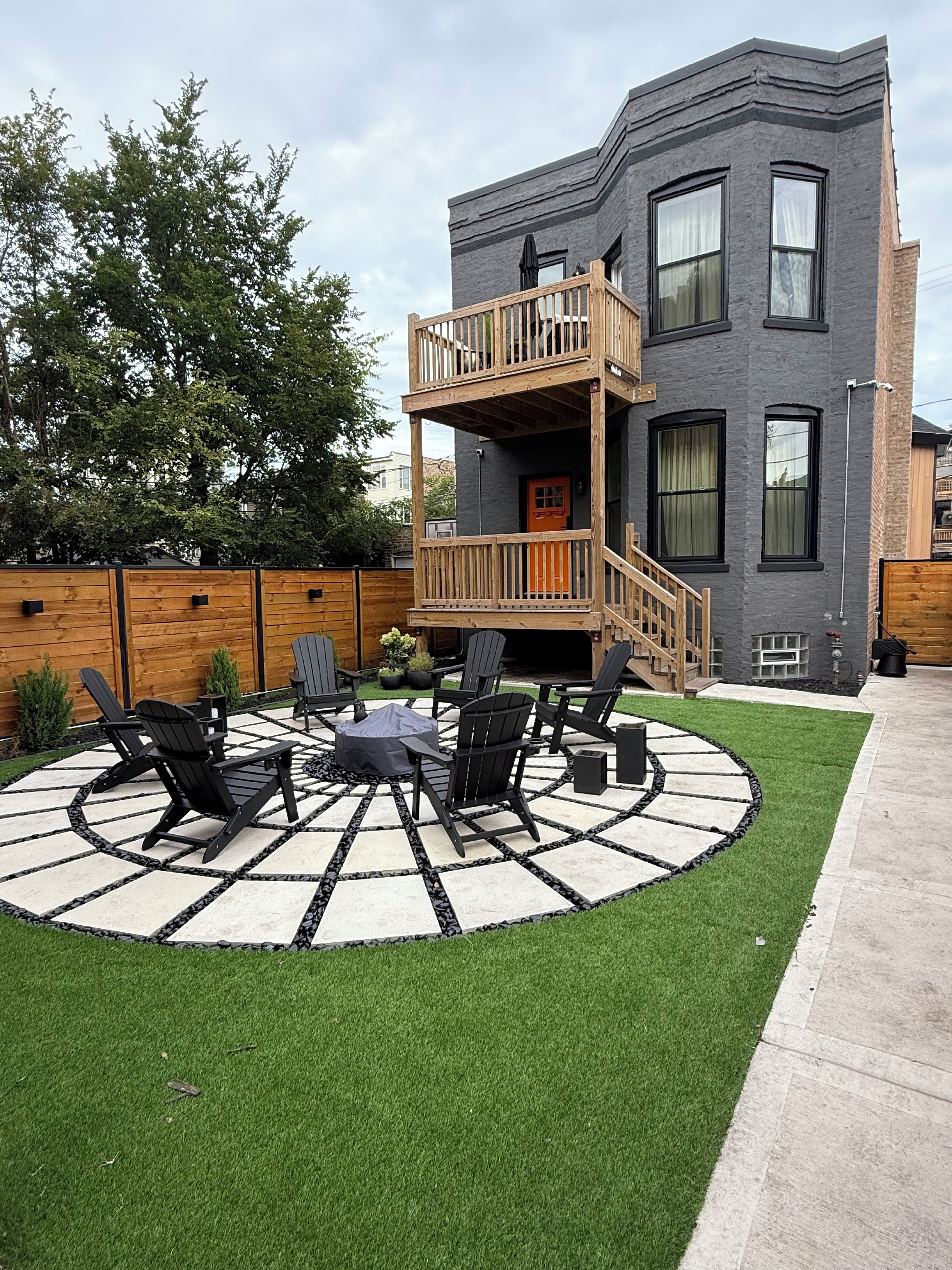 Een gebouw met twee verdiepingen, een balkon, een rond zitgedeelte buiten met stoelen en een tafel, en een verzorgd gazon.