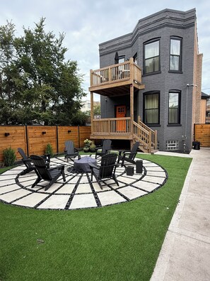Un bâtiment à deux étages doté d’un balcon, d’un espace extérieur circulaire aménagé avec des chaises et une table, et d’une pelouse bien entretenue.
