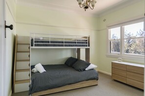 A bunk bed with a ladder, a desk, and a window with a view of trees. - Pearl Cottage – Charming Coastal Retreat (Ulladulla)