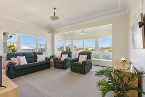 Ein geräumiges Wohnzimmer mit großem Fenster, einem grünen Sofa, zwei Sesseln und einem kleinen Tisch.