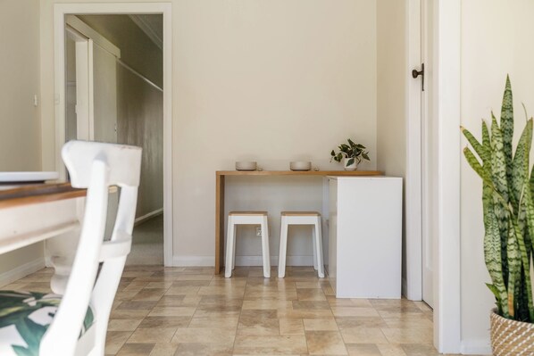 Eine kleine Küchenzeile mit Kühlschrank, zwei Hocker, einem Holztisch und einem Blumentopf.