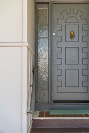 A grey door with a decorative metal knocker and a textured glass panel. - Pearl Cottage – Charming Coastal Retreat (Ulladulla)