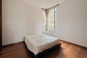 Une chambre avec un lit simple, une fenêtre avec des rideaux et une vue sur un bâtiment à l’extérieur.