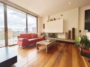 Un salon moderne avec un canapé rouge, une table basse en verre et une grande fenêtre donnant sur la ville.