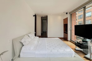 A modern bedroom with a large bed, a television, and a sliding glass door leading to a balcony. - Bright 2BR Apartment in Virrey with Private Jacuzzi & AC (Bogotá)