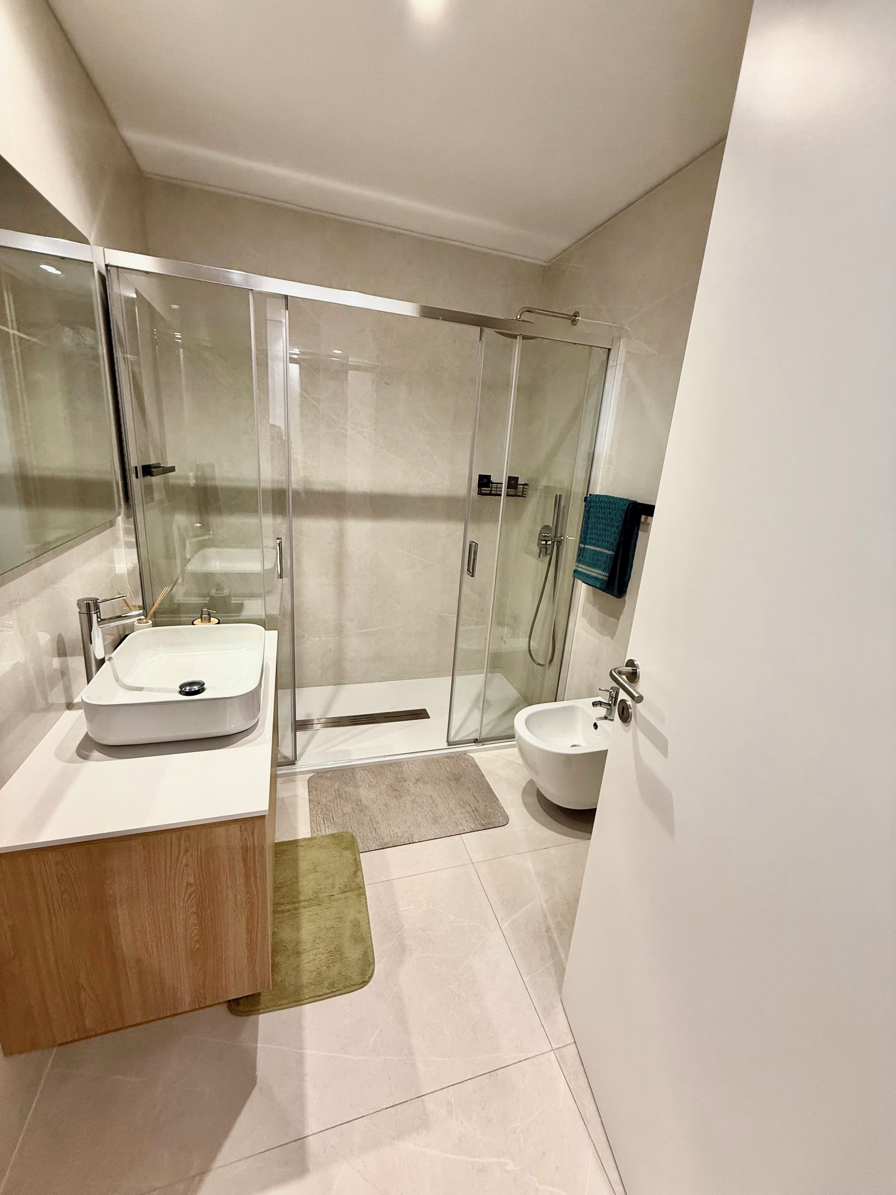 Ein modernes Badezimmer mit einer gläsernen Duschkabine, einem hölzernen Waschtisch und einem Bidet.