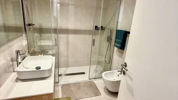 Ein modernes Badezimmer mit einer gläsernen Duschkabine, einem hölzernen Waschtisch und einem Bidet.