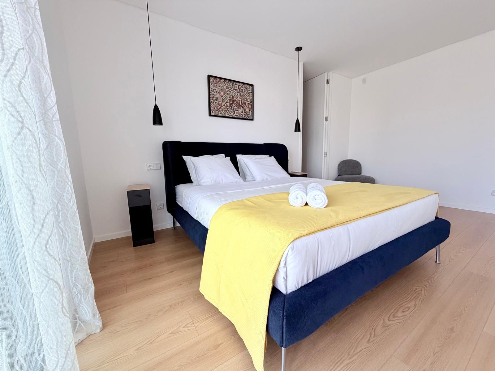 Een moderne slaapkamer met een bed, nachtkastjes, een stoel en een kunstwerk aan de muur.