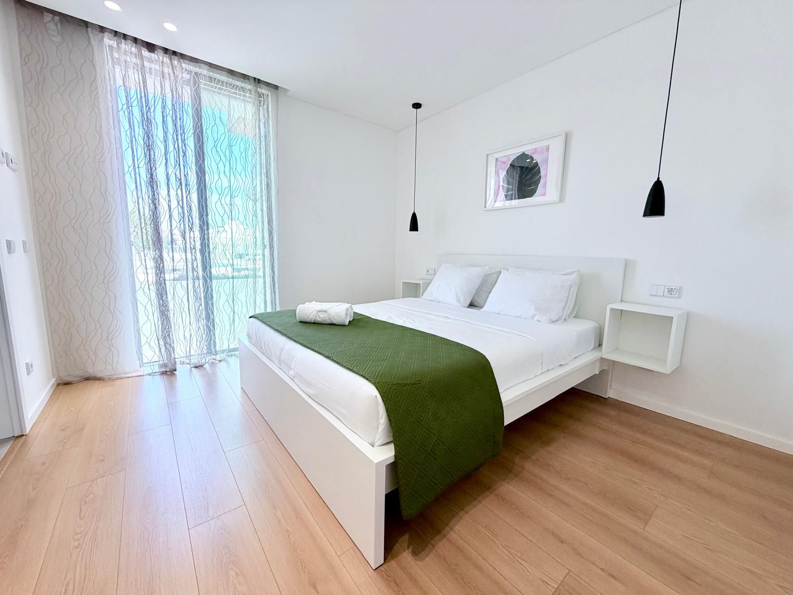 A modern bedroom with a bed, bedside tables, a window with curtains, and a wall-mounted picture.