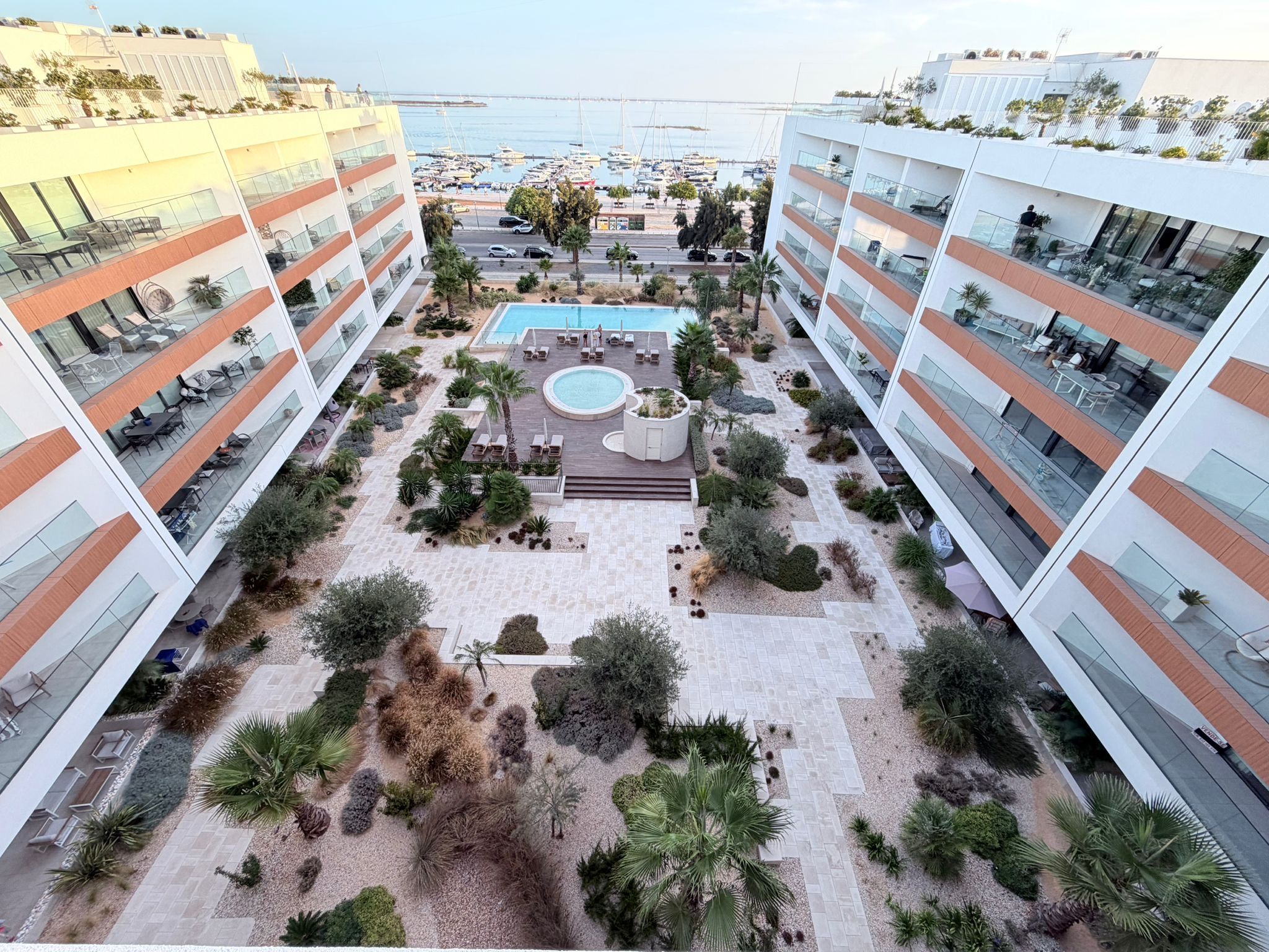 A hotel courtyard with a swimming pool, lounge areas, and a view of the sea.