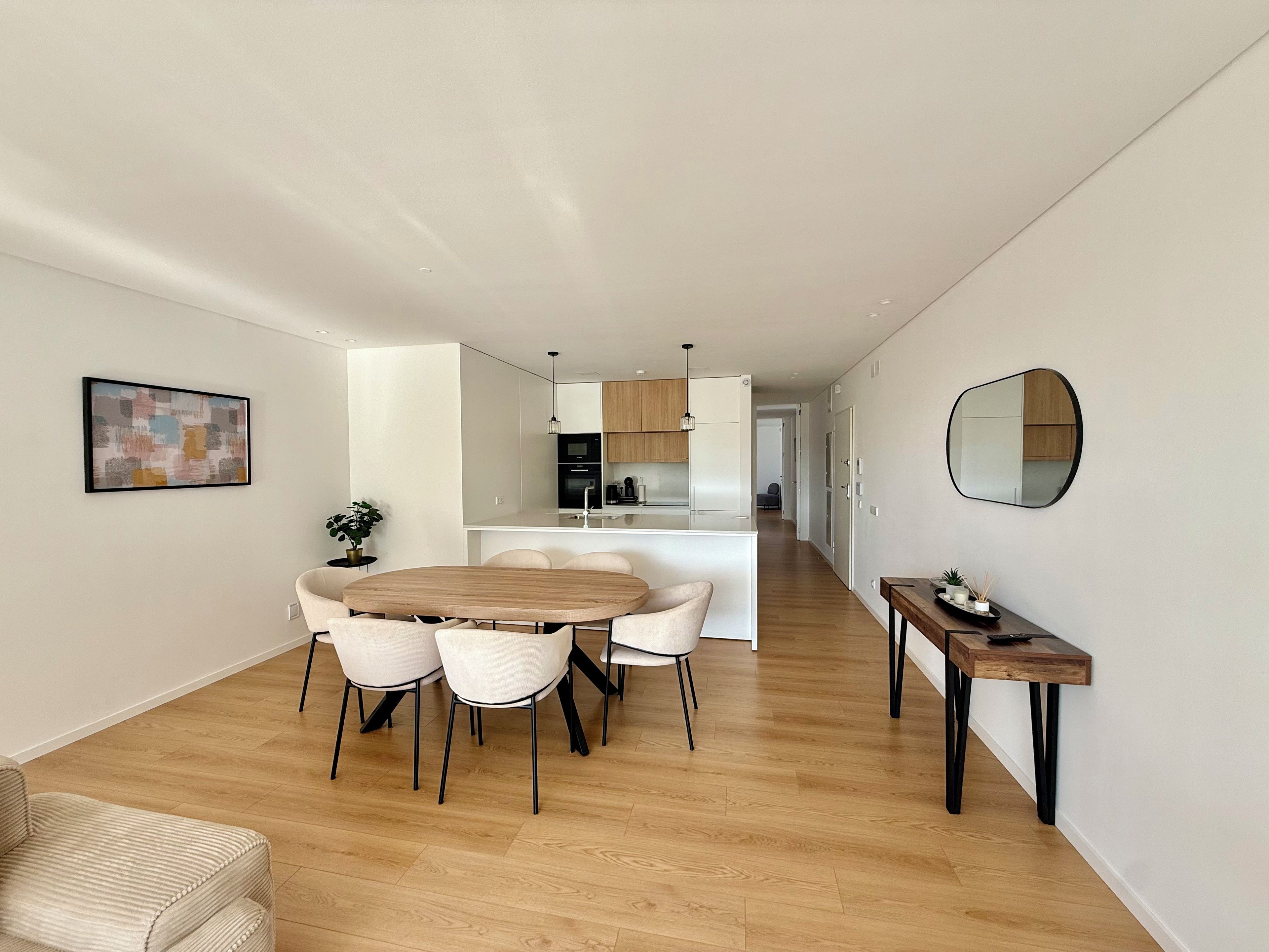 A modern kitchen with white cabinets, a central island, and a dining area with a wooden table and chairs.