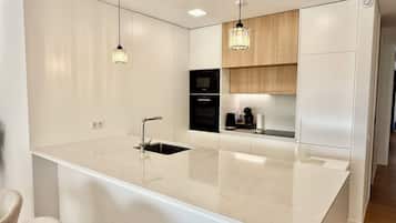 Une cuisine moderne dotée d’un îlot central, d’appareils électroménagers intégrés et de luminaires suspendus.