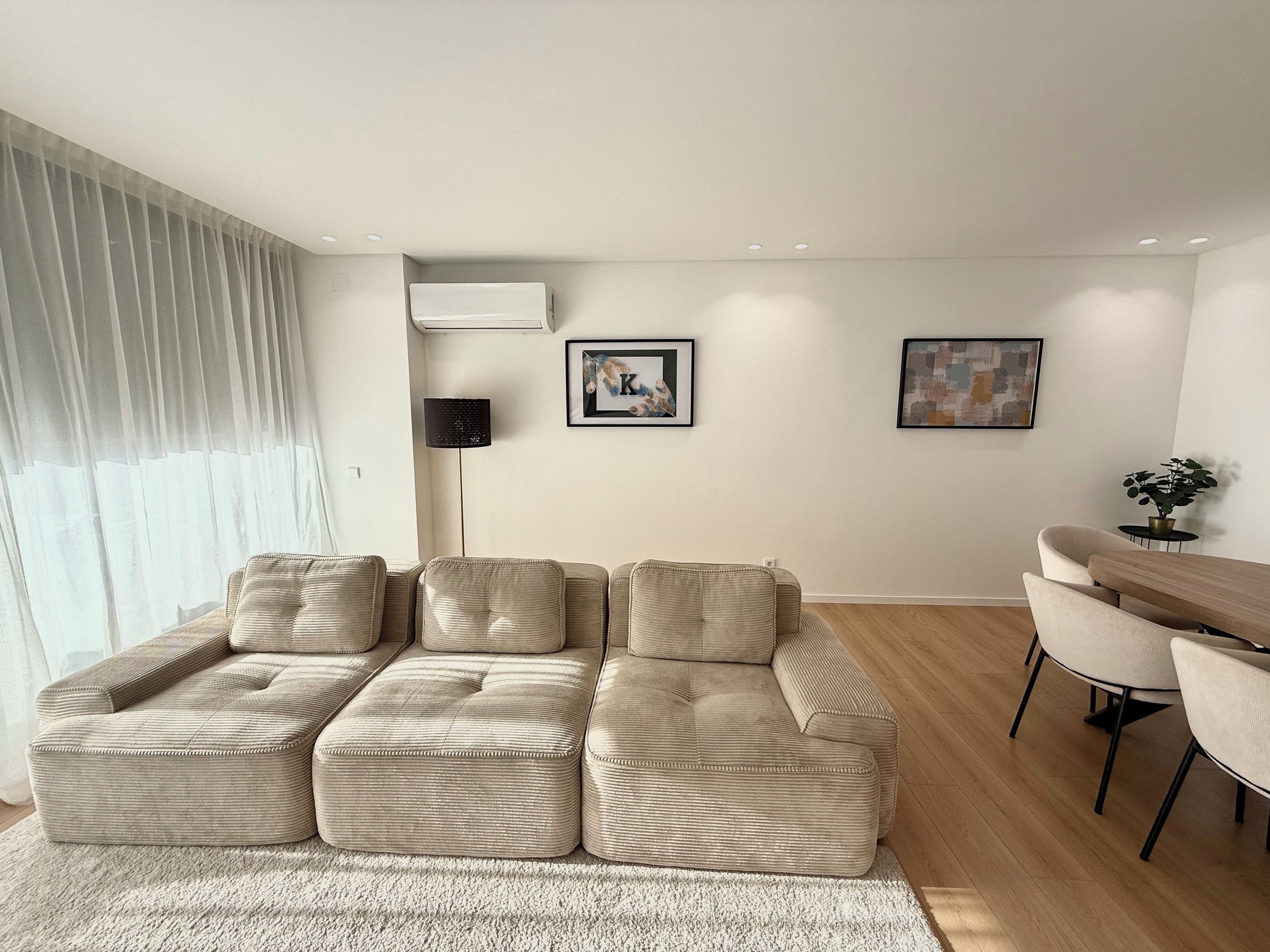 Una sala de estar moderna con un sofá modular, un comedor con una mesita y sillas, y obras de arte en las paredes.