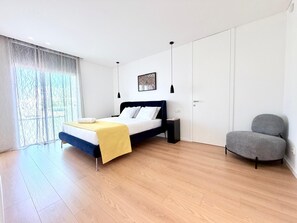 A modern bedroom with a bed, bedside table, and a chair. - Luxury family apartment with a view of the estuary (Olhão)