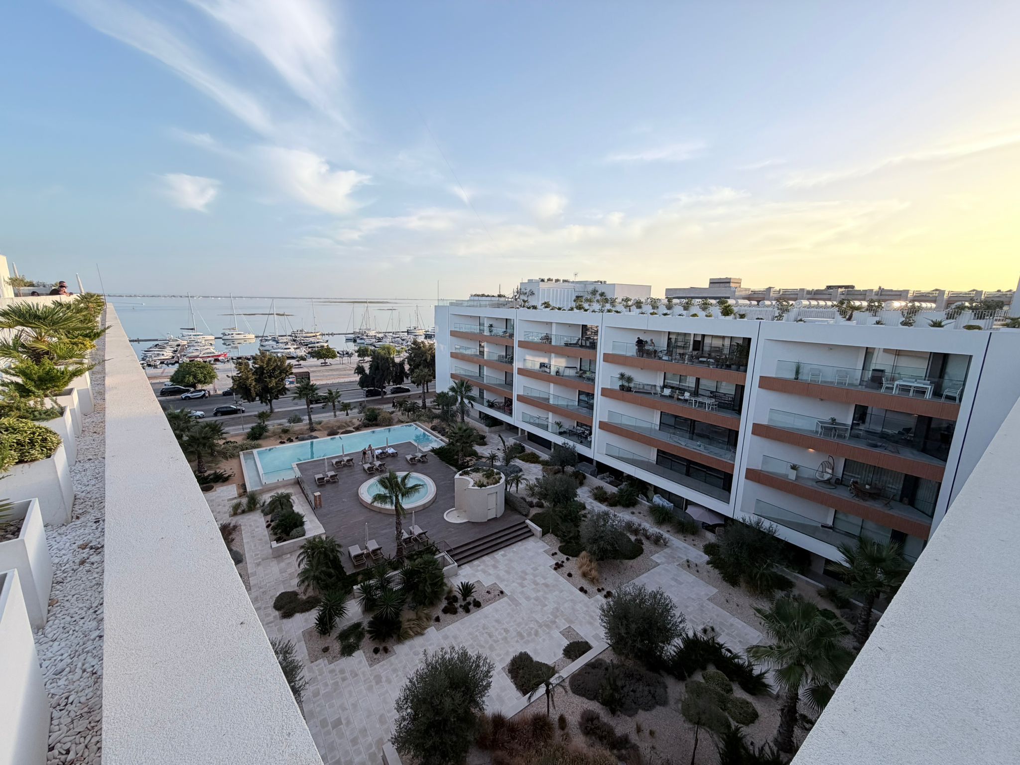 A modern building with multiple balconies overlooking a marina and a pool area.
