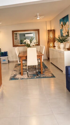A dining area with a wooden table, white chairs, a decorative rug, and a ceiling fan. - Villa Dushi 2bedroom King/Pool 3 min to Palm Beach (Noord)