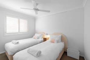 Une chambre avec deux lits simples, un ventilateur de plafond, une fenêtre avec des stores et un radiateur.